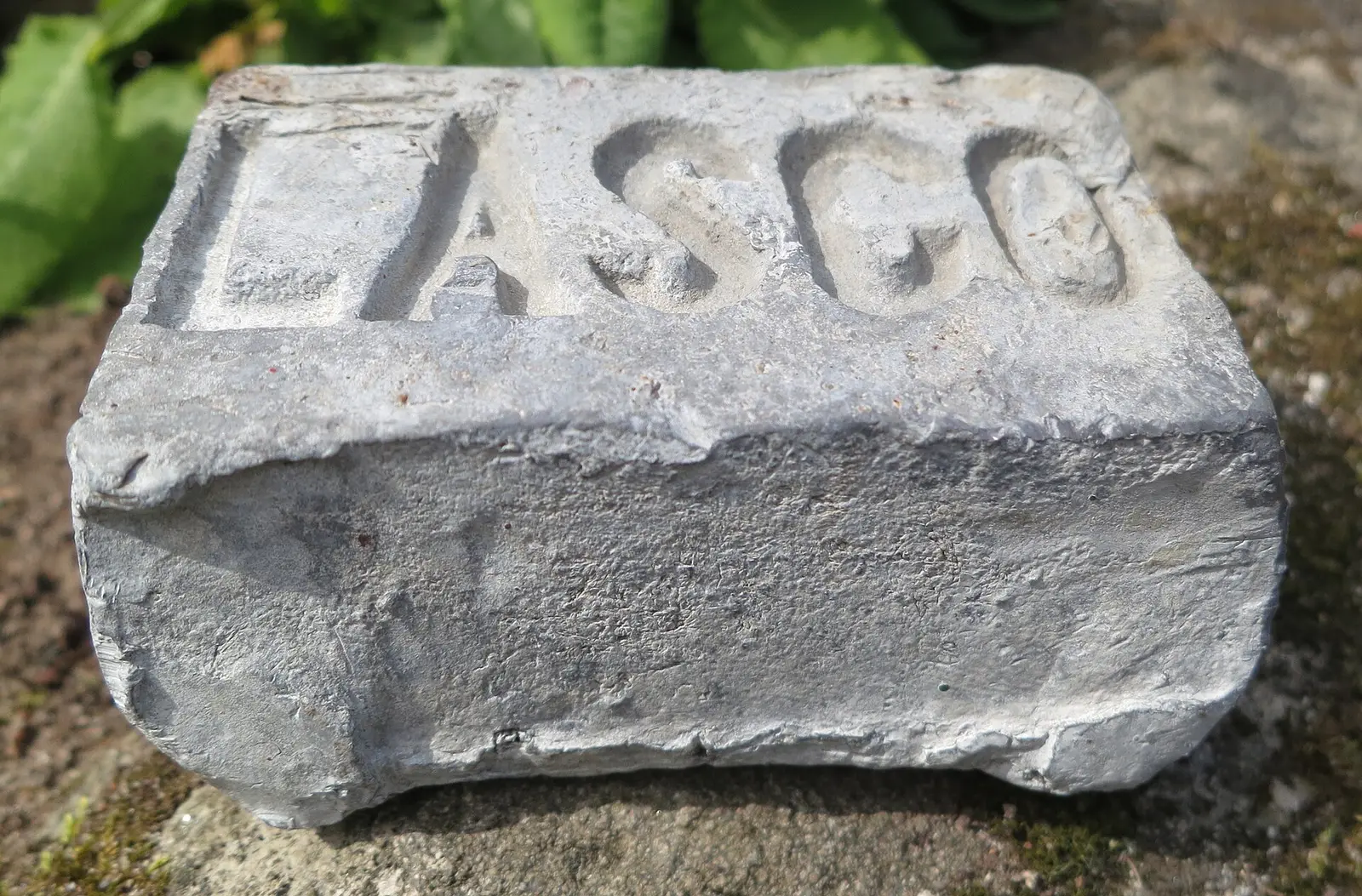 A lead ingot with letters cast into its top face, resting on stone.